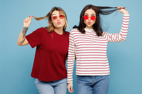 Young couple two friends women wear red glasses casual clothes together look camera with duckface play with hair isolated on pastel plain light blue cyan background studio portrait. Lifestyle concept.