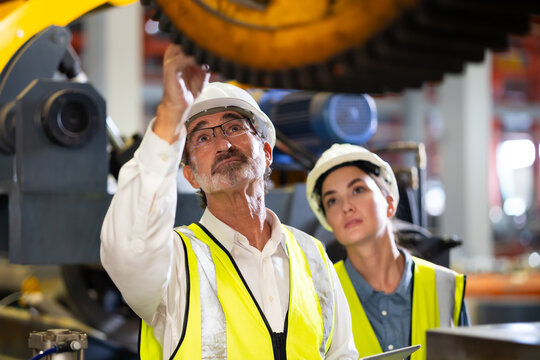 Senior manager man Factory worker training to woman colleague on production line in Heavy Industry Manufacturing Facility. Instructor with Trainee working at factory.