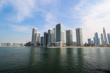 Naklejka premium Dubai waterfront skyline with modern skyscrapers A scenic view of Dubai’s waterfront featuring modern skyscrapers, reflecting on calm waters under a clear blue sky. 