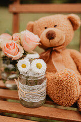 Teddy sitzt auf Holzstuhl mit Rosen und Gänseblümchen auf einer Wiese - Geburtstag, Freude, Liebe