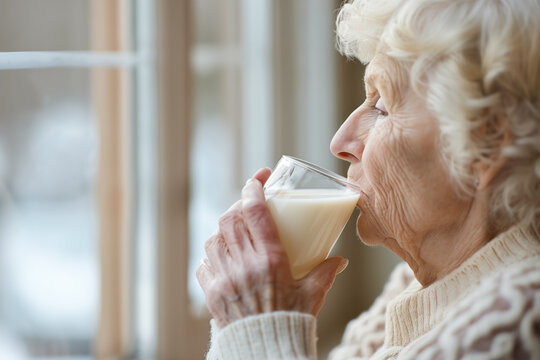 Drinking milk. Elderly woman enjoys a glass of milk while gazing out the window. Older people and milk benefits