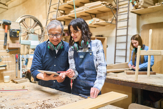 Experienced craftsman mentoring young apprentice in busy lumberyard
