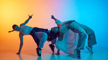 Synchronized movements. Two young women in casual clothes dynamically performing hip hop against...