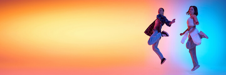 Dynamic image of two young energetic women in motion, hip hop dancer performing against gradient studio background in neon light. Concept of modern dance style, hobby, active lifestyle, youth culture