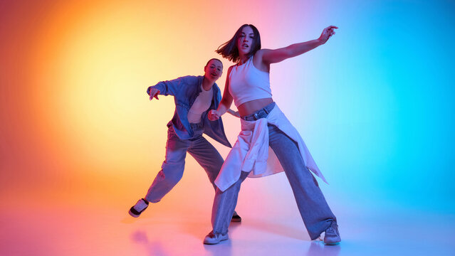 Modern hip hop fusion captured in motion with two dancers dancing against gradient studio background in neon light. Concept of modern dance style, hobby, active lifestyle, youth culture