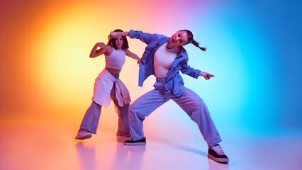 Powerful hip hop energy radiating from stylish young dancers in casualwear against gradient studio background in neon light. Concept of modern dance style, hobby, active lifestyle, youth culture