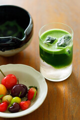 Cup of fresh matcha tea, green tea and colorful peach fruit shape Plating balls, Thailand style dessert on wooden table.