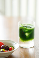 Cup of fresh matcha tea, green tea and colorful peach fruit shape Plating balls, Thailand style dessert on wooden table.