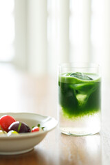 Cup of fresh matcha tea, green tea and colorful peach fruit shape Plating balls, Thailand style dessert on wooden table.