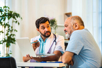 Indian doctor and senior patient discussing diagnosis on laptop in a cozy clinic setting