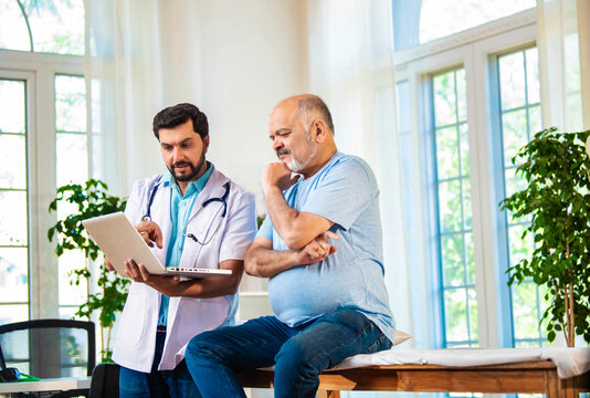 Indian doctor and senior patient discussing diagnosis on laptop in a cozy clinic setting