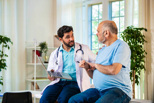Indian Asian doctor explaining wrist pain causes and treatment to elderly patient in cozy clinic