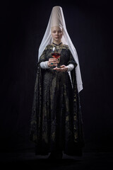Young noblewoman in renaissance dress holding wine glass with focused expression, looking forward...