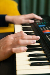 Obraz premium Woman's hands skillfully playing a vintage synthesizer keyboard, crafting electronic music in a cozy studio adorned with a yellow sofa and a soft green curtain. Vertical photo