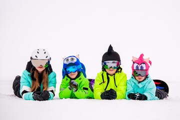 group of children and teenagers lie on the snow at a ski resort against a backdrop of white snow.