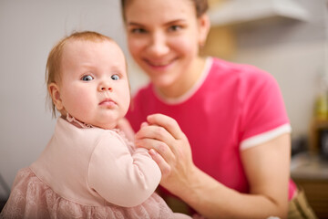 Joyful mother holding curious baby girl in bright room
