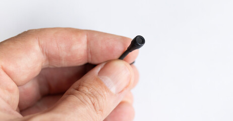 A close-up of a hand holding a small black wired microphone against a white background. The tiny...