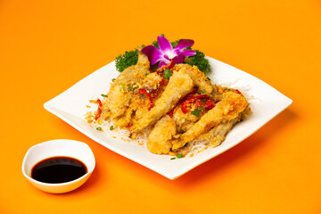 Salt and pepper fried fish with soy sauce, tomato and coriander served in plate isolated on orange background side view of hong kong food