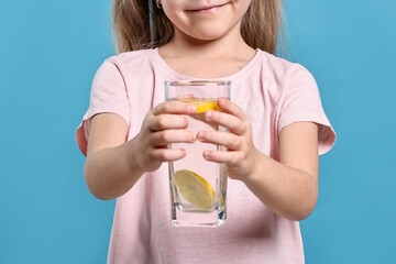 Girl with glass of lemonade on light blue background, closeup. Refreshing drink