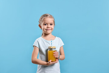 Girl with mason jar of orange juice on light blue background, space for text. Refreshing drink