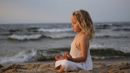 Blond child practicing meditative yoga on sunset lit seashore, embodying inner peace through mindful movement near gentle ocean waves. Concept for children meditation and unity with nature