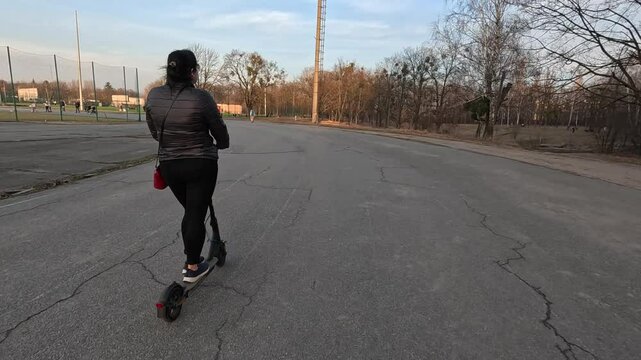 A woman rides an electric scooter on asphalt.