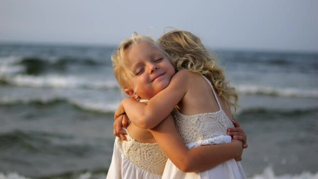 Two young blonde sisters wearing white dresses are embracing on a beach with the ocean in the background, enjoying a tender moment of affection. concept Childrens devoted love