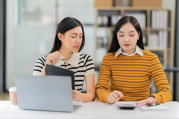 Two young Asian women wearing headphones and working intently on their laptops and tablets. Remote working.