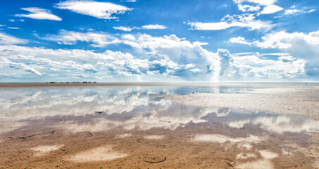 blue sky with clouds reflected in shallow water at beach