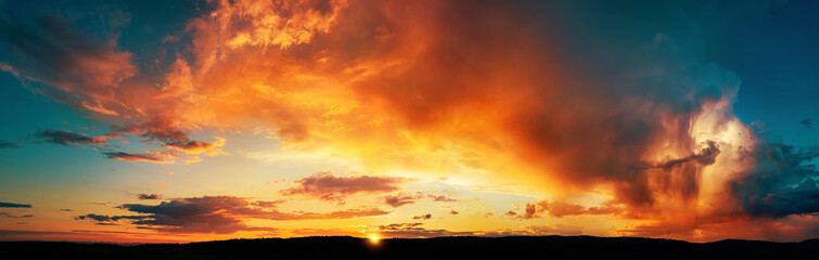 Dramatic storm clouds lit in vivid orange and yellow colors at sunset. A panoramic weather shot 