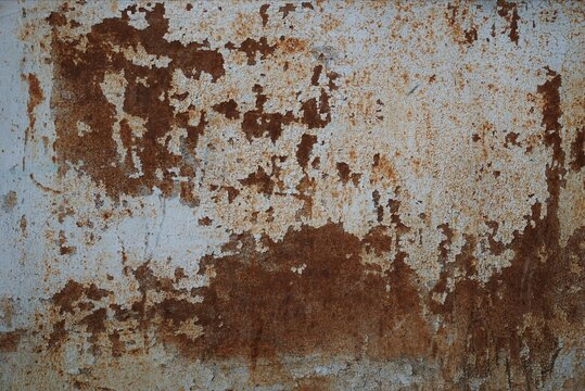 Close-up photo of a weathered metal surface covered with flaking light blue-gray paint and patches of orange-brown rust. Cracks, stains and corroded areas create an authentic grunge, industrial look.