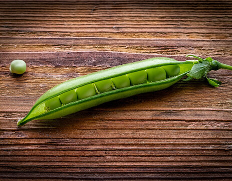 A single sugar snap pea pod with visible seeds resting on a textured wooden background