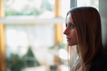 Side Profile of a Woman Looking Thoughtfully Outdoors Through a Window..