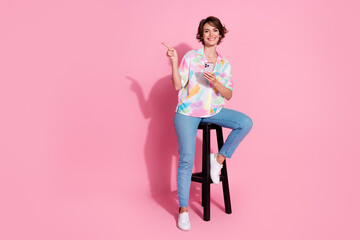 Full size photo of pretty young lady sit stool phone direct finger empty space wear shirt isolated...