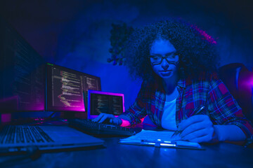 Young female programmer working on code in a modern workspace with multiple monitors, showcasing focus