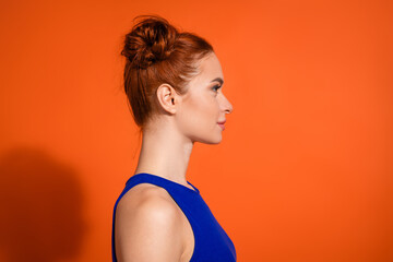 Obraz premium Side profile of a young woman with red hair in a bun against an orange background, wearing a blue top and showcasing casual summer fashion