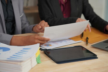 Office workers work together at desks with laptop computers and digital tablets, analyzing data in various documents. before summarizing and presenting to the meeting