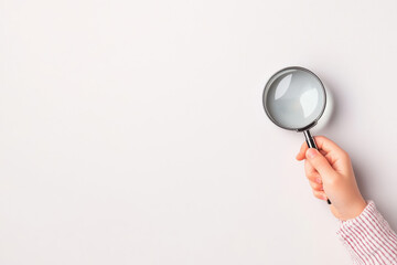 A close-up view of a hand holding a magnifying glass against a blank background, perfect for inquiry and exploration themes.