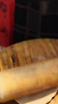 Hands of man using rolling pin to flatten dough into thin round sheet on wooden table, preparing homemade Indian flatbread in kitchen. Close-up view
