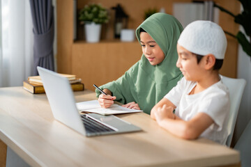Asian Muslim boy and girl do homework together at home, Student electronic learning with happiness. Childs study by looking at laptop seriously.