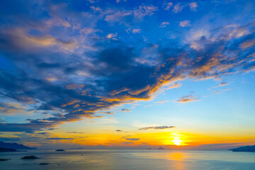 View of horizon over ocean in the distance there are islands and mountains with lilac tinted clouds texture before sunrise early in the morning