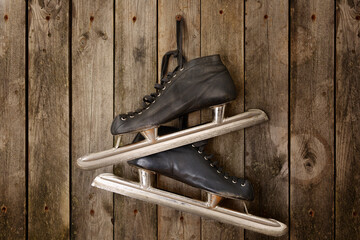 Black old skates hanging from laces on a wooden wall