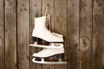 White figure ice skates hanging on weathered wooden wall