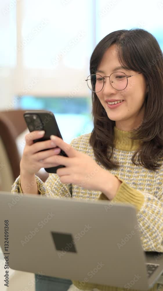 Poster vertical video of asian woman smiling and wearing glasses while using smartphone to search internet,