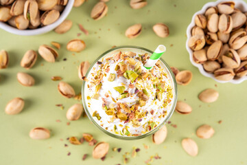 Fototapeta premium Pistachio milkshake, healthy diet protein cocktail, non-dairy whipped shake with vegan pistachio milk, whipped plant-based cream, sprinkled with nuts, on light green background