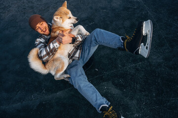 Smiling, embracing the pet. Man with Akita Inu dog is on the ice with skates in winter
