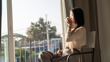 Relaxed young woman enjoying coffee by the window at home