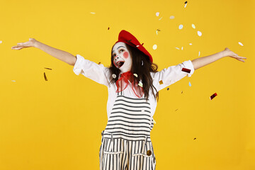Happy girl dressed like mime under falling confetti on yellow background. Surprise party