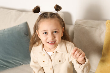 Fototapeta premium Cute little girl with missing tooth on sofa indoors. Waiting for tooth fairy