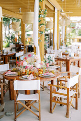 Round festive table with a bright bouquet of flowers and white chairs stands on the restaurant terrace